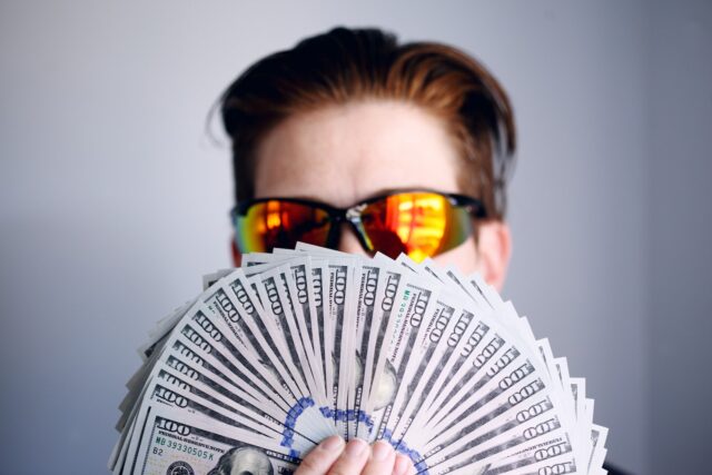 man in black framed sunglasses holding fan of money for down payment on a home